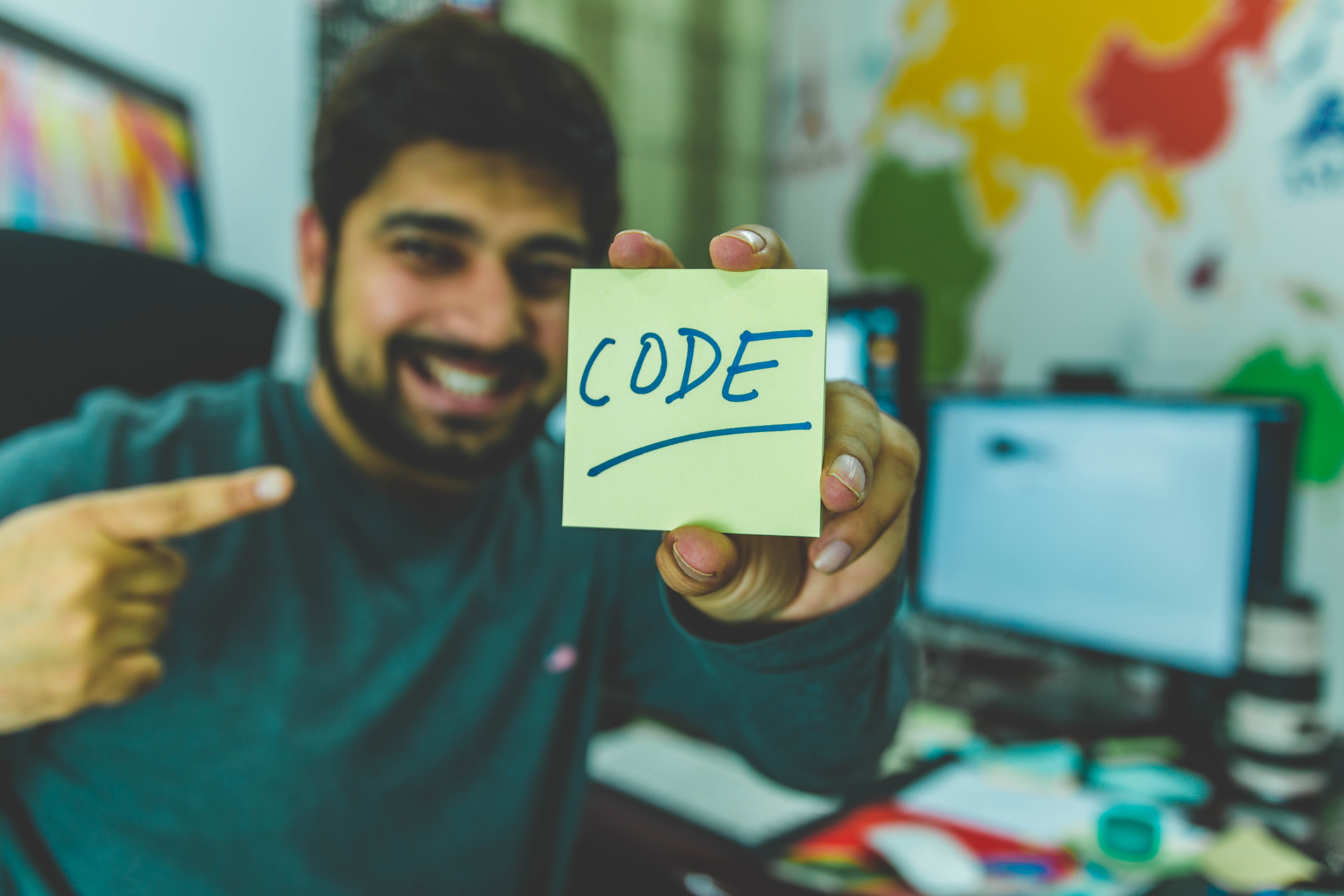 Man in grey sweater holding sticky note which says code